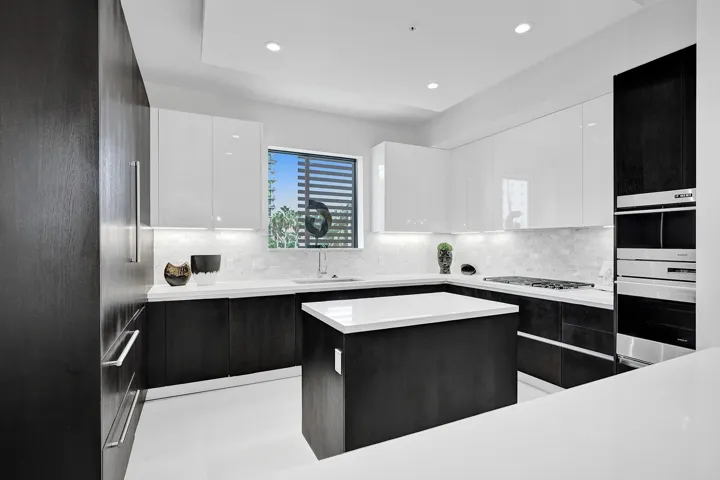 Modern kitchen featuring dark wood-finish lower cabinetry, white high-gloss upper cabinetry, a central island with a white countertop, stainless steel appliances, and a mosaic tile backsplash