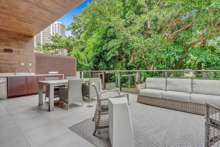Outdoor patio featuring an integrated kitchen with a stainless steel sink, built-in grill, wood-finish cabinetry, and a glass railing