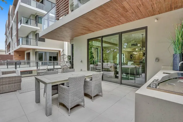 Spacious private patio featuring large format tile flooring, an outdoor kitchen with integrated grill, and a wood-finish ceiling accent