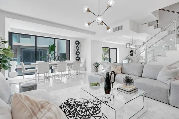 Spacious open-concept living area featuring a modern chandelier, polished tile flooring, and a glass-paneled staircase with a metal handrail