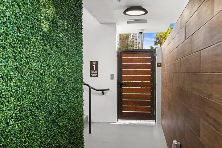 Exterior entryway featuring a faux hedge wall, a wood-slat gate with a metal frame, and wood-finish paneling