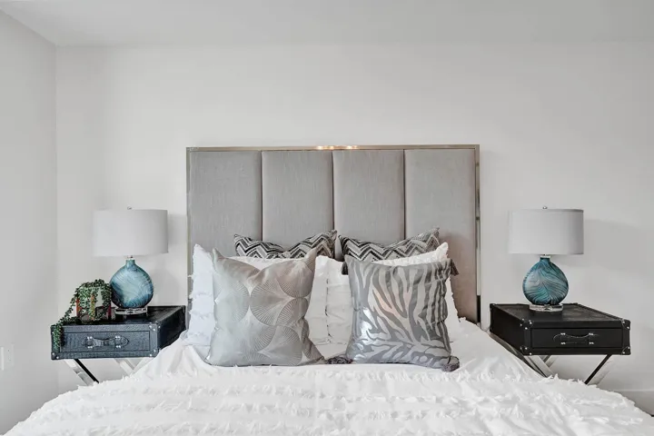 Bed featuring an upholstered headboard with chrome trim, white walls, and built-in lighting fixtures