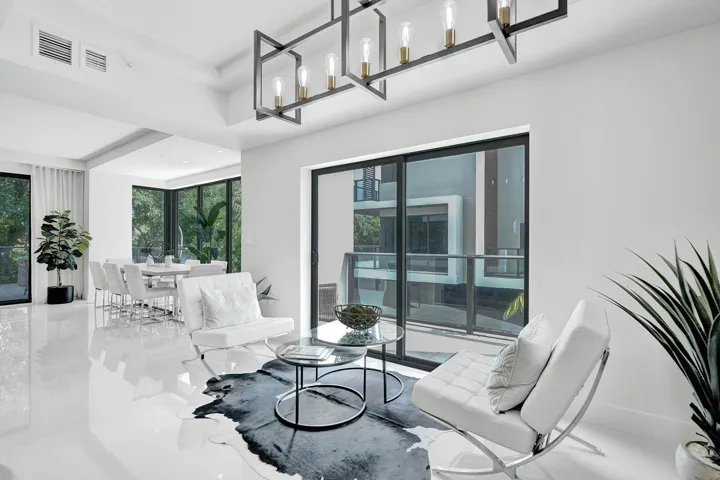 Spacious living area featuring polished white flooring, a modern linear chandelier with exposed bulbs, and a sliding glass door opening to a private balcony