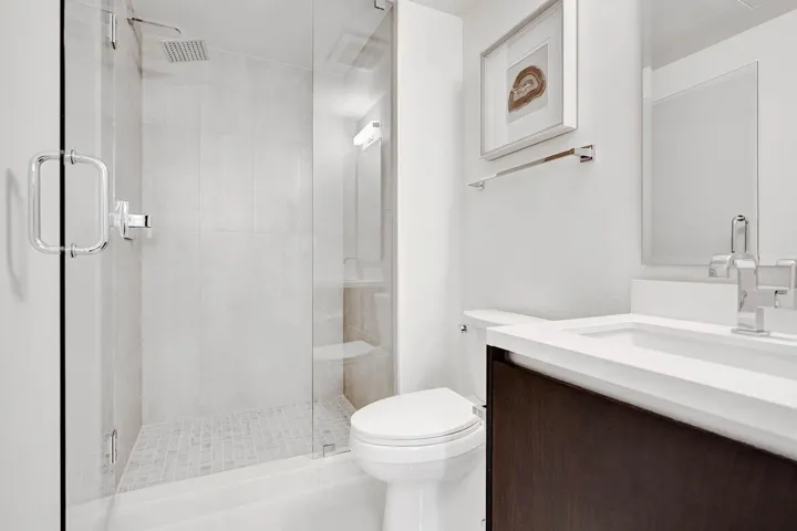 Bathroom featuring a glass-enclosed shower with a rainfall showerhead, white wall tiling, and a mosaic floor
