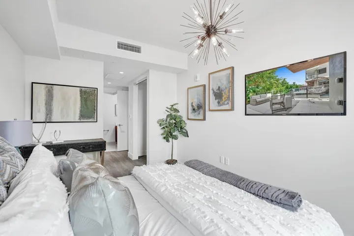 Bright and serene primary bedroom featuring crisp white bedding, wood-finish flooring, and abundant natural light