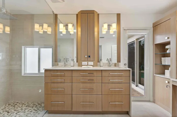 Spa-inspired primary bathroom featuring a custom wood-finish double vanity with dual sinks, polished nickel hardware, and an illuminated mirror surround