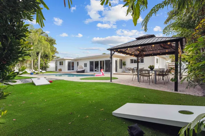 Expansive backyard oasis featuring manicured lawn, mature landscaping with specimen trees, and a modern pergola-covered entertaining area with dining setup