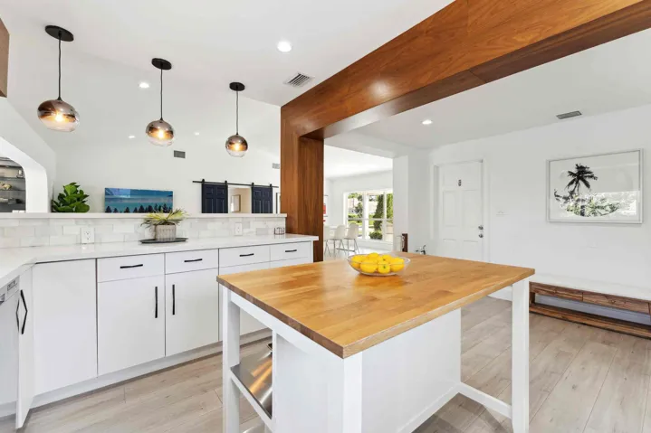 Modern kitchen featuring white cabinetry, a substantial wood-topped island with storage, pendant lighting with copper-finish shades, and a large wood beam architectural element
