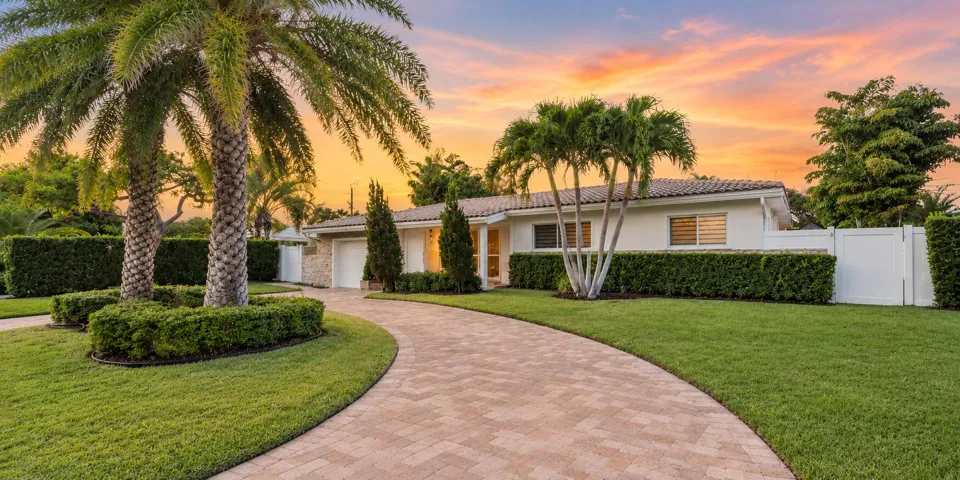 Elegant single-story residence showcasing a curved brick paver driveway, mature palm tree landscaping, and manicured lawn with established hedging