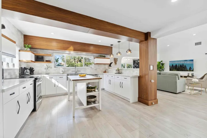 Contemporary kitchen and open-concept living space featuring white cabinetry with hardware accents, a large center island with open shelving, and stainless steel appliances