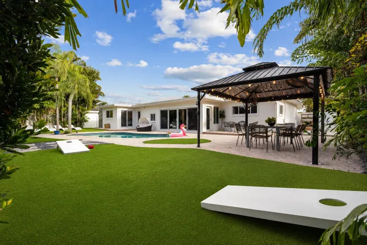 Expansive backyard featuring a manicured lawn, mature landscape plantings, and a modern pergola structure with integrated seating area