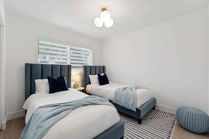 Bright interior space featuring a window with horizontal blinds, wood-finish flooring, and a modern ceiling light fixture