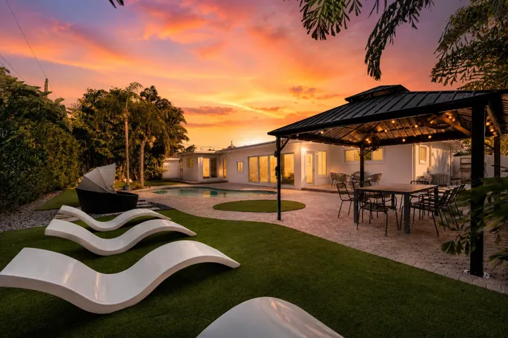 Luxurious outdoor entertaining space featuring a manicured lawn, curved lounge seating, and a pergola-covered dining area with integrated lighting