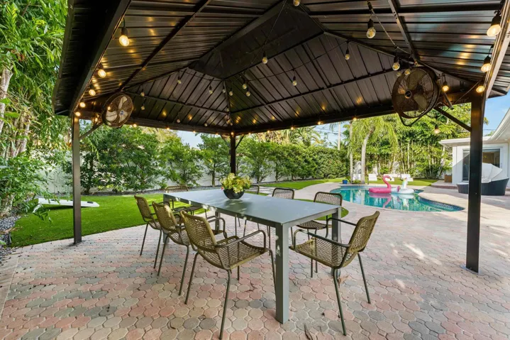 Sophisticated outdoor entertaining space featuring a sturdy metal pergola with integrated overhead lighting and ceiling fans, anchored by a spacious dining table with seating for six