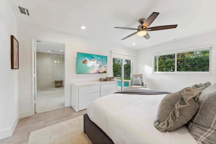 Bright primary bedroom featuring a wood-finish plank floor, ceiling fan with integrated lighting, and abundant natural light from dual windows