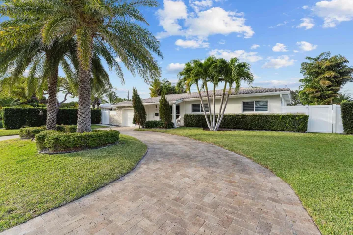 Elegant residence featuring a curved brick paver driveway, mature palm trees, and lush manicured landscaping