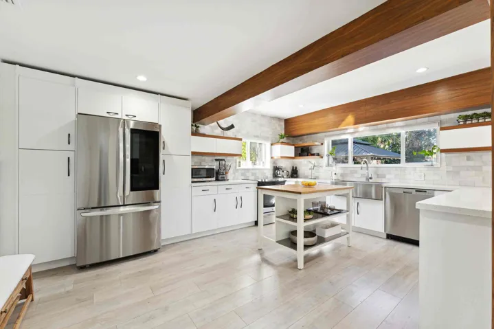 Spacious kitchen featuring vaulted ceilings with exposed wood beams, stainless steel appliances, white cabinetry, and a tile backsplash