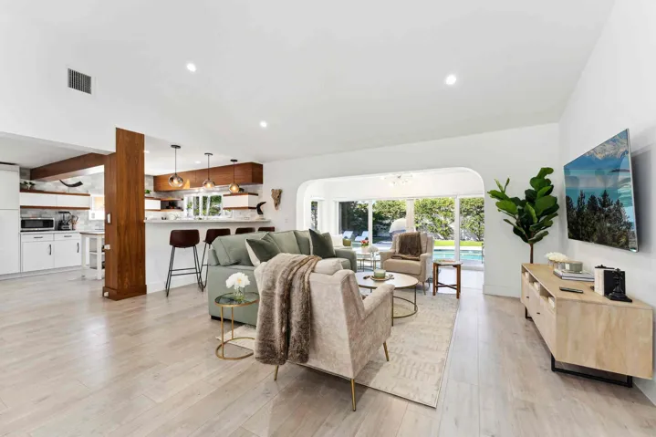 Open-concept living space featuring a wood-finish plank floor, white vaulted ceiling with recessed lighting, and abundant natural light from multiple windows and glass doors