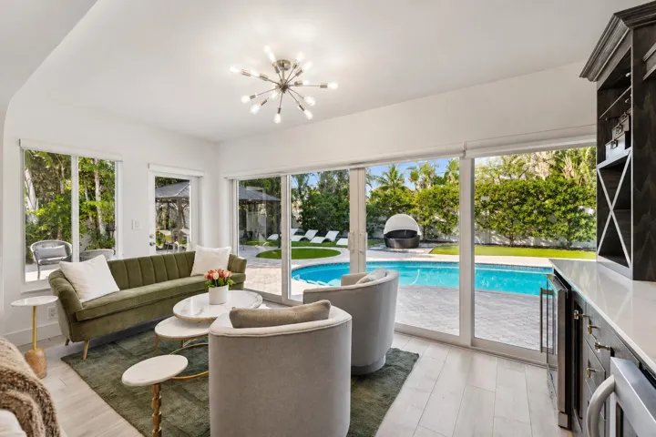 Sophisticated poolside living space featuring expansive sliding glass doors, light wood-finish flooring, and seamless indoor-outdoor connectivity