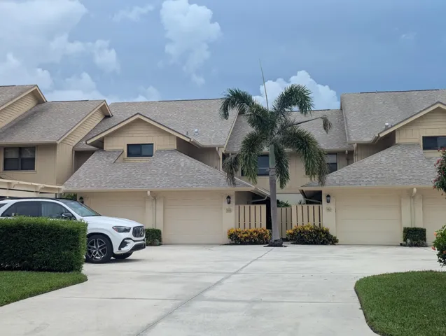 Tan-toned exterior featuring multiple garage doors, gabled rooflines, a palm tree, and manicured landscaping