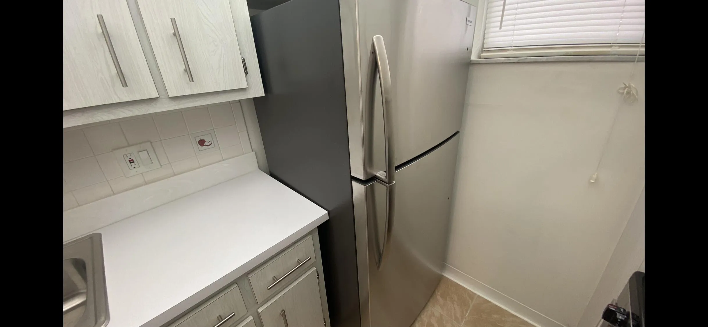 Kitchen featuring light wood-finish cabinetry with brushed nickel hardware, a brand new stainless steel refrigerator, white countertops, and a ceramic tile backsplash