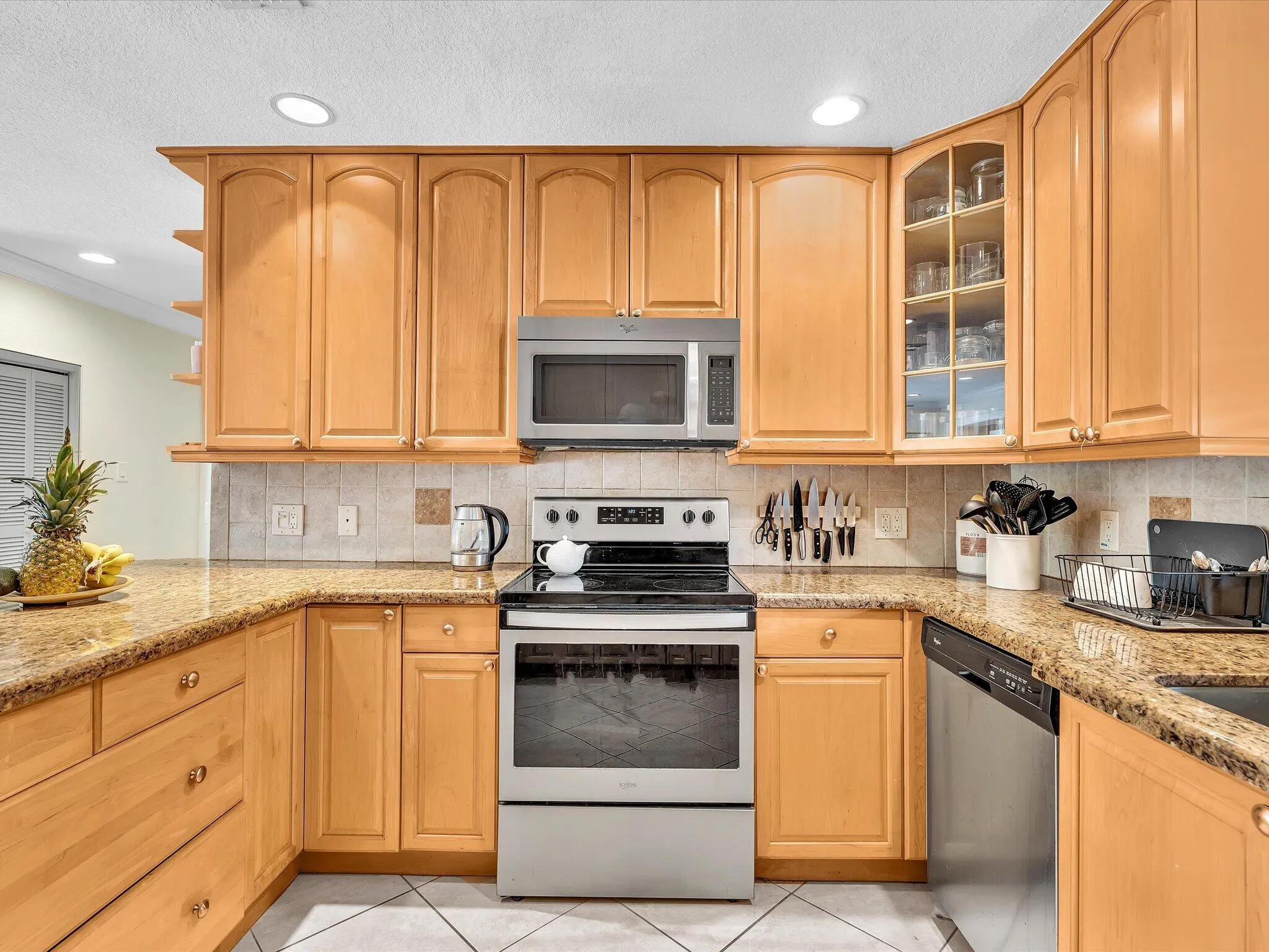 U-shaped kitchen featuring wood-finish cabinetry, granite countertops, and a tile backsplash
