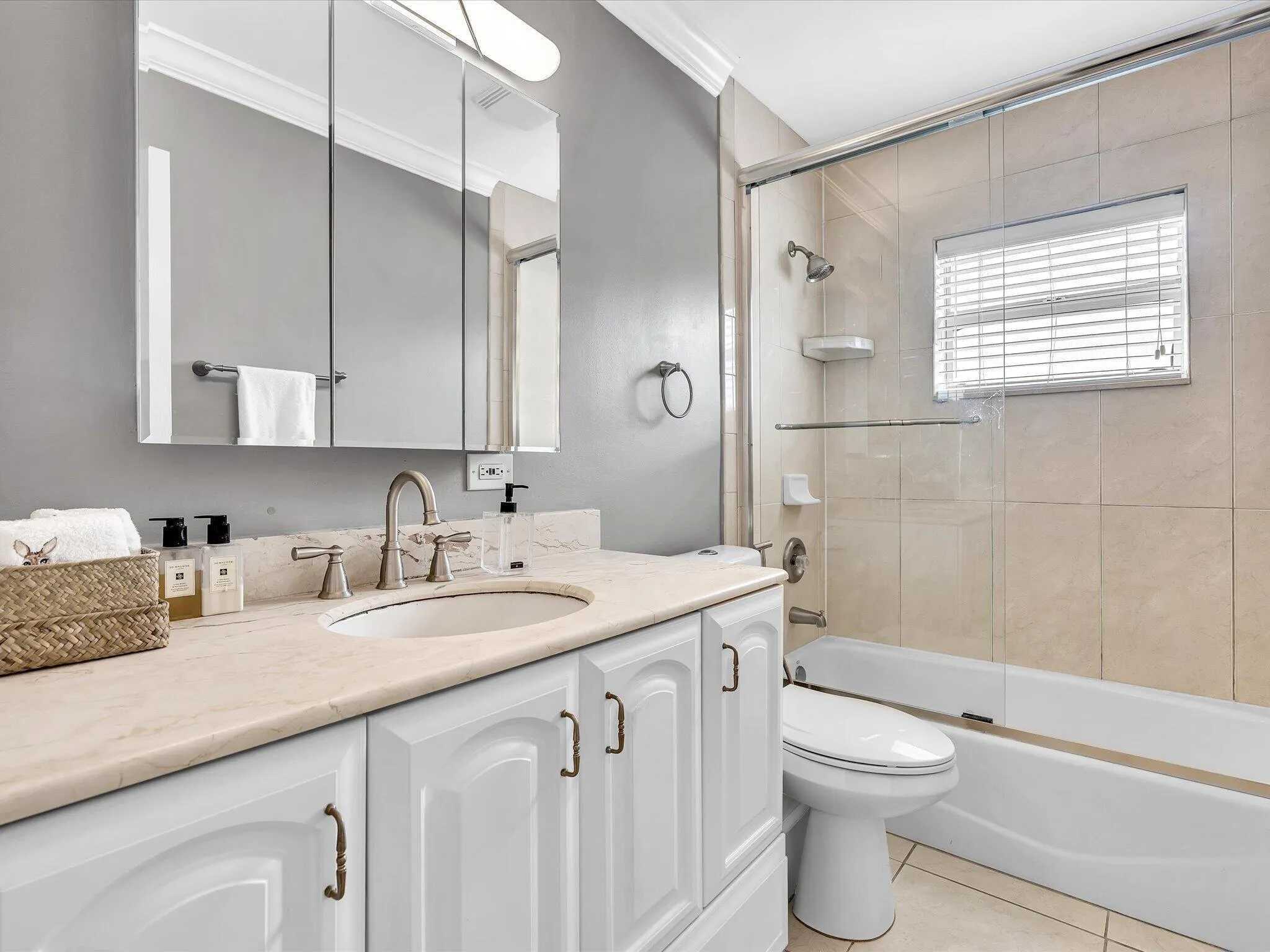 Spa-inspired bathroom featuring a dual-sink vanity with white cabinetry, light wood-finish countertops, and an illuminated mirror with integrated lighting