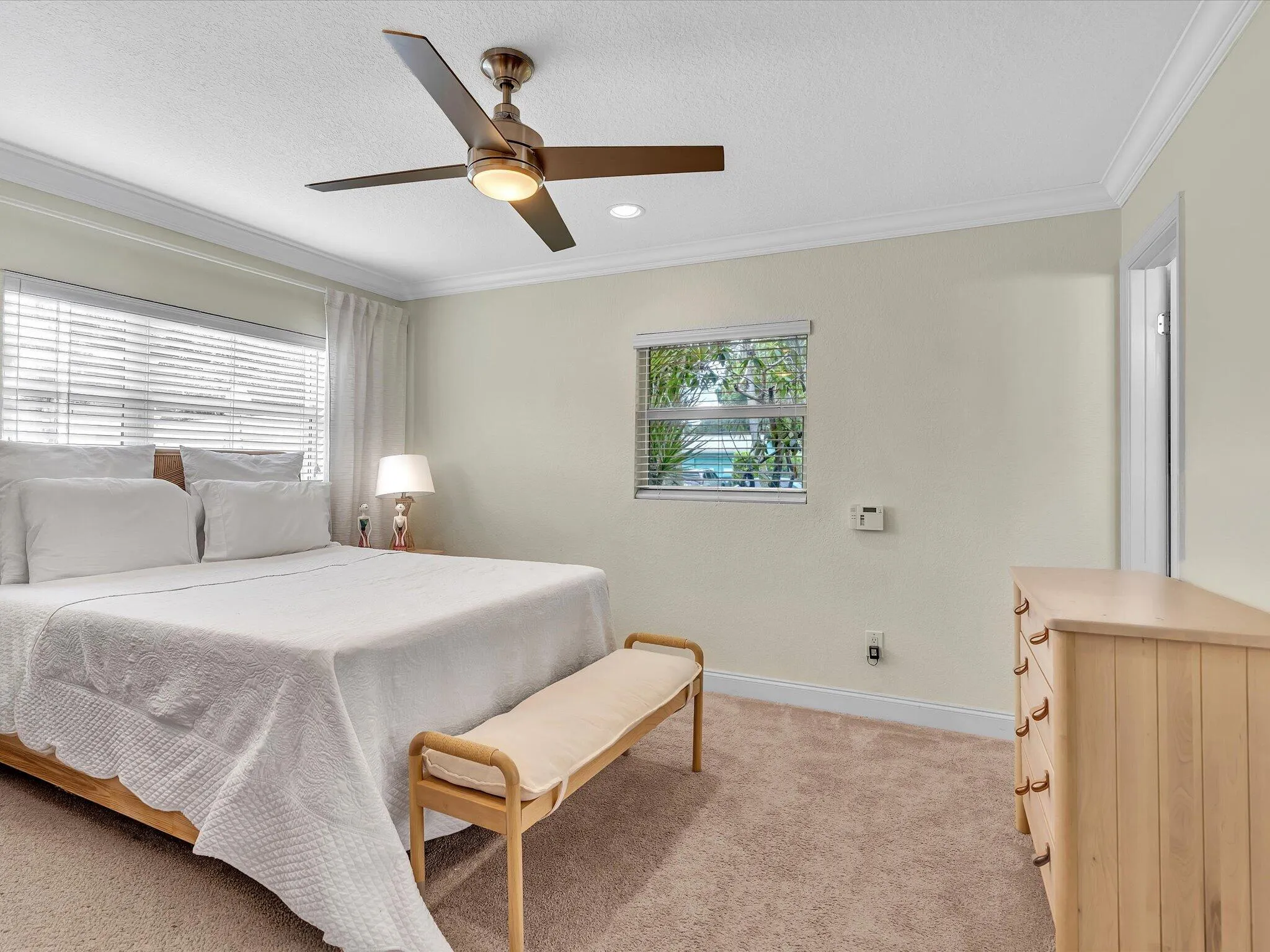 Celling fan with integrated lighting, two windows with blinds, and neutral tone carpeting