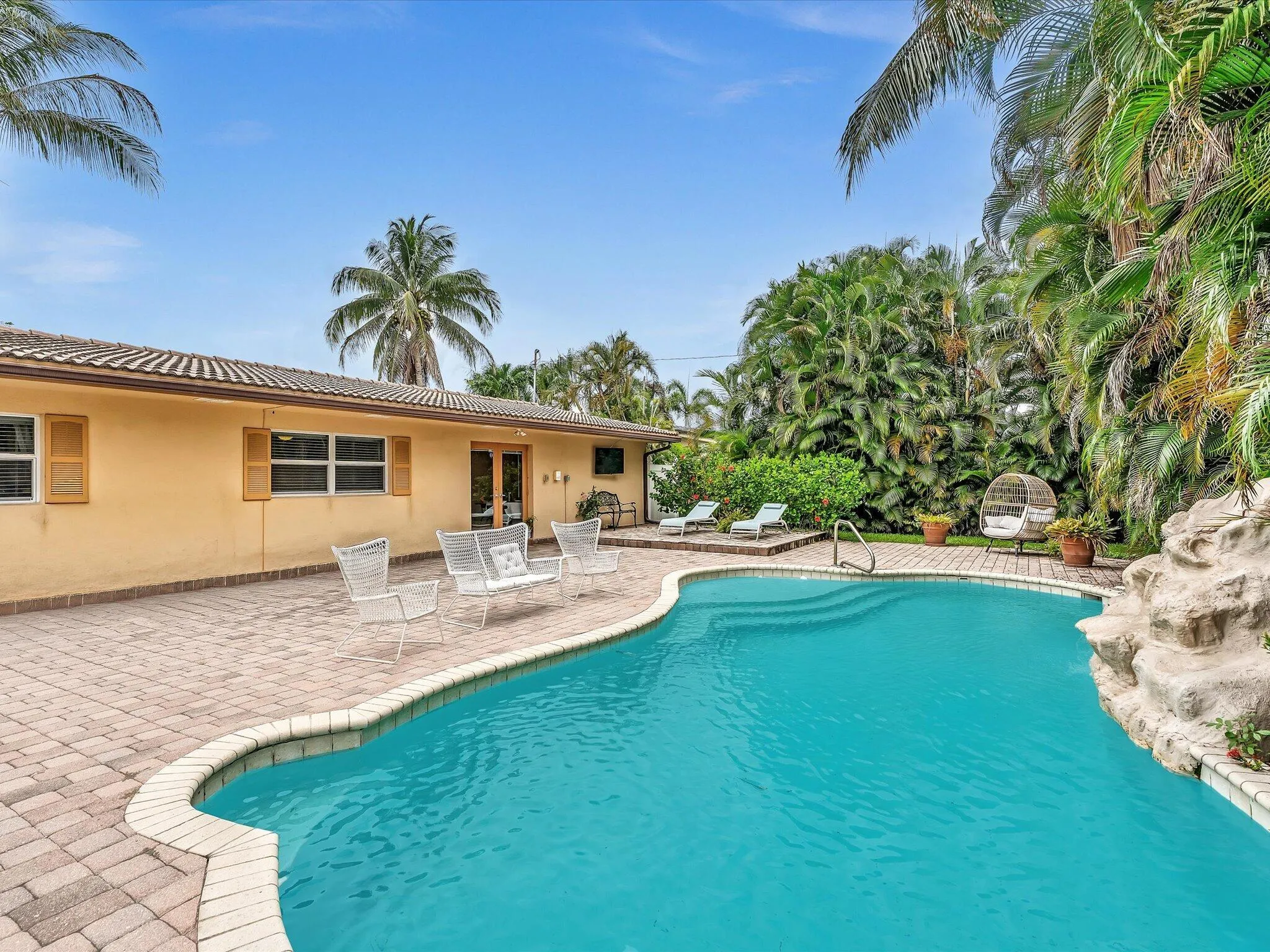 Outdoor swimming pool with integrated steps, surrounded by a paver patio and lush tropical landscaping