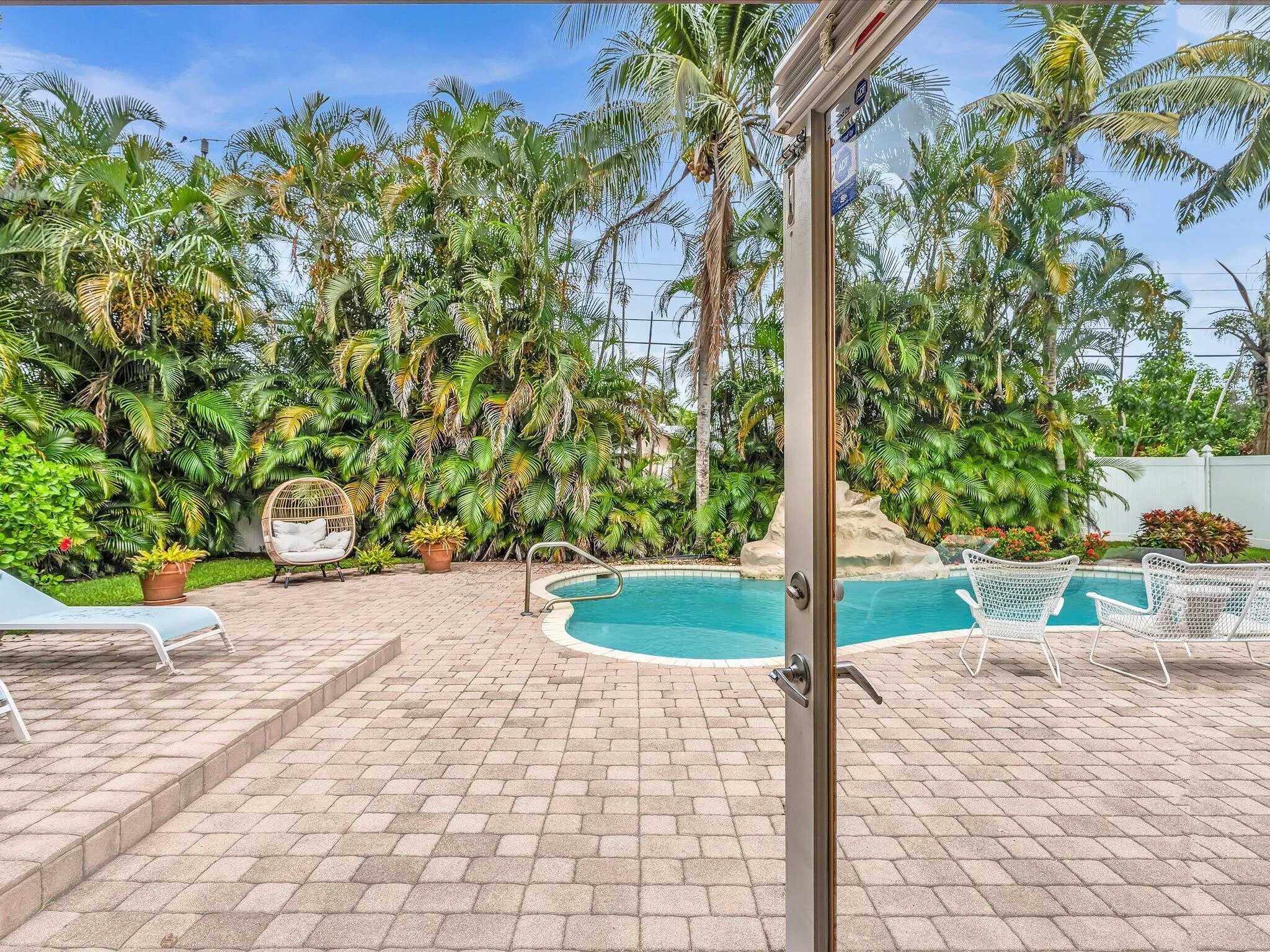 Paved patio with integrated steps, private swimming pool with rock feature, and extensive perimeter foliage