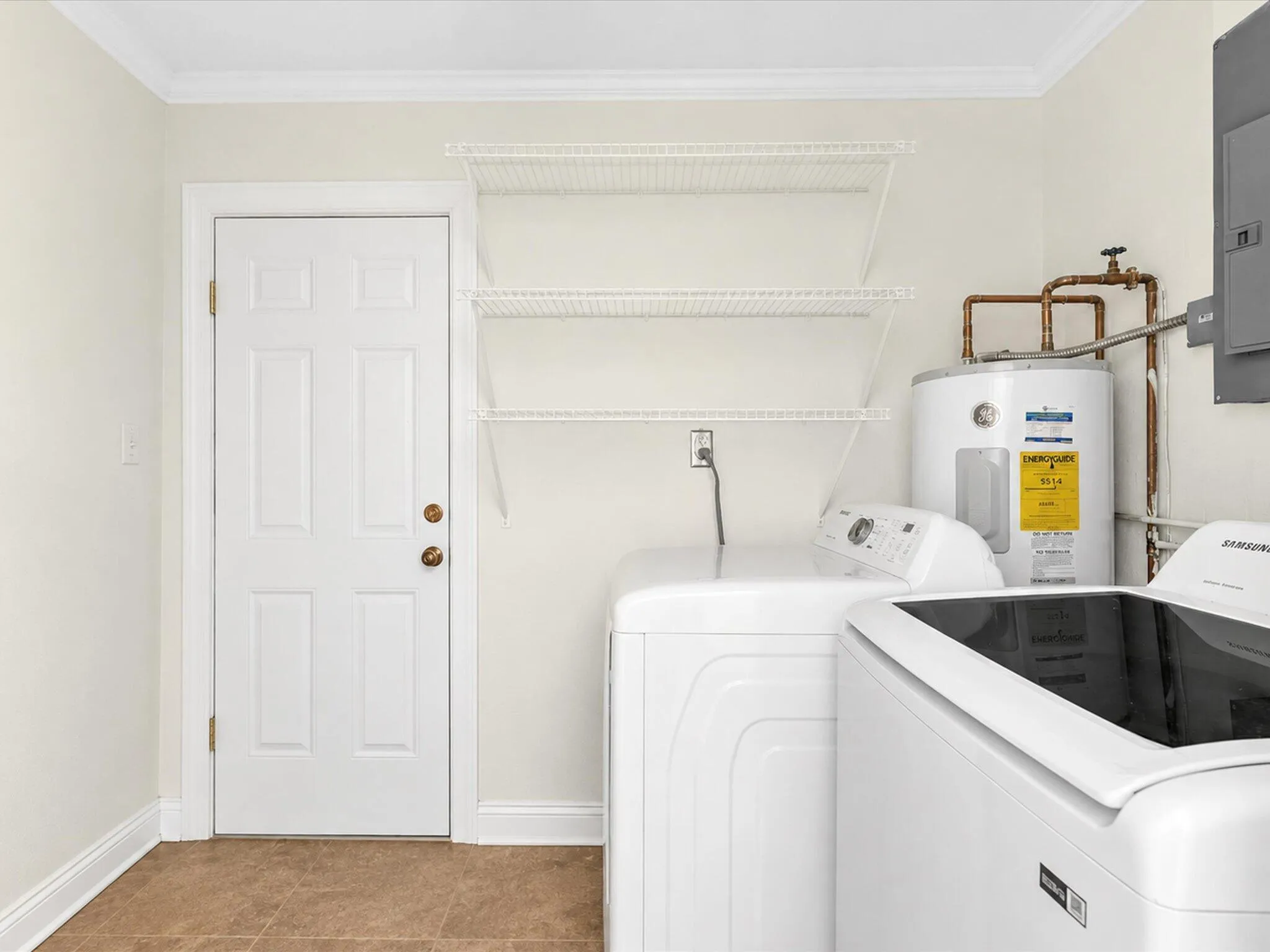 Utility area featuring tile flooring, a paneled door, crown molding, and built-in shelving