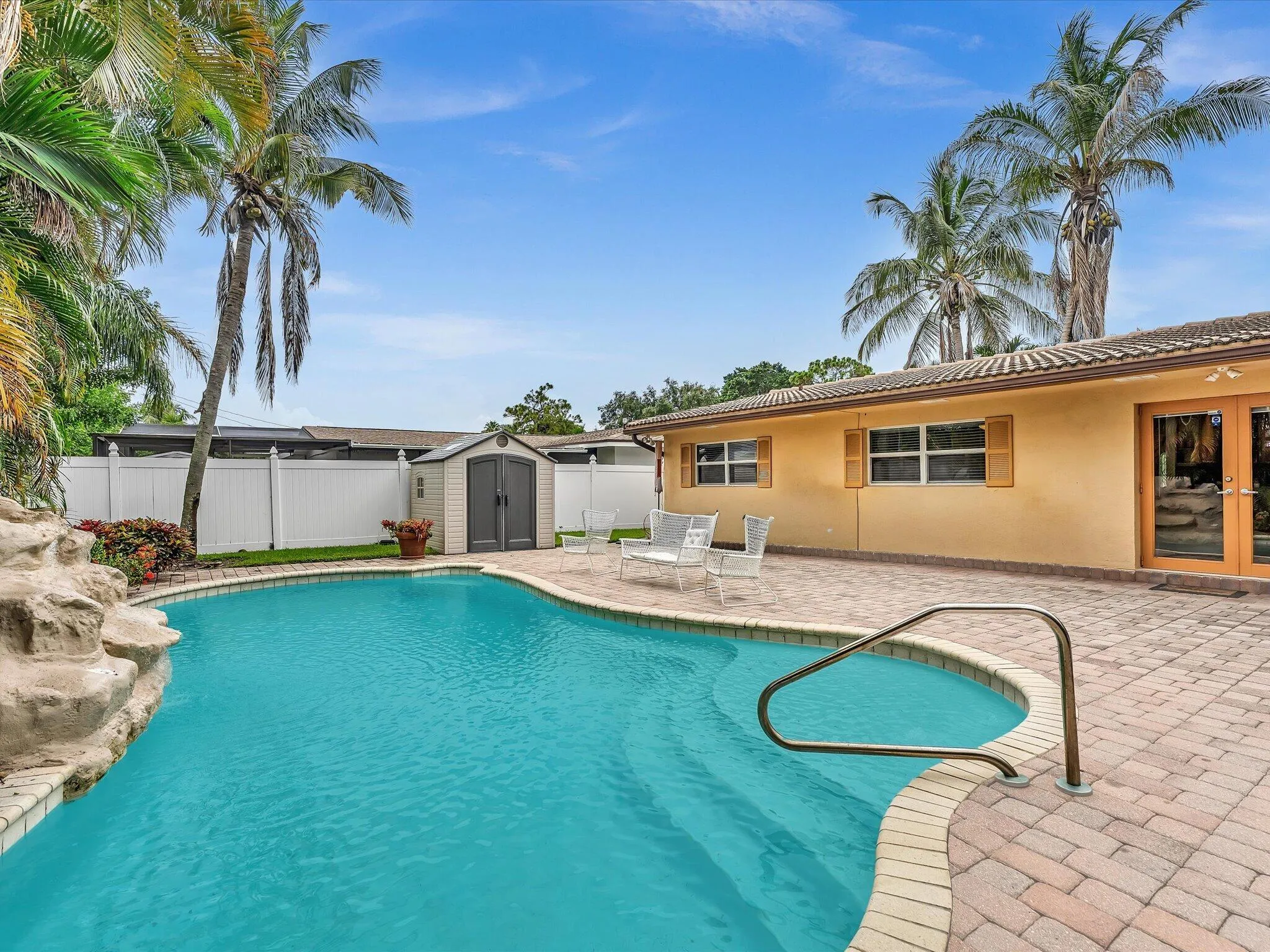 Resort-style pool with a rock water feature, paver patio, privacy fencing, and an exterior storage shed