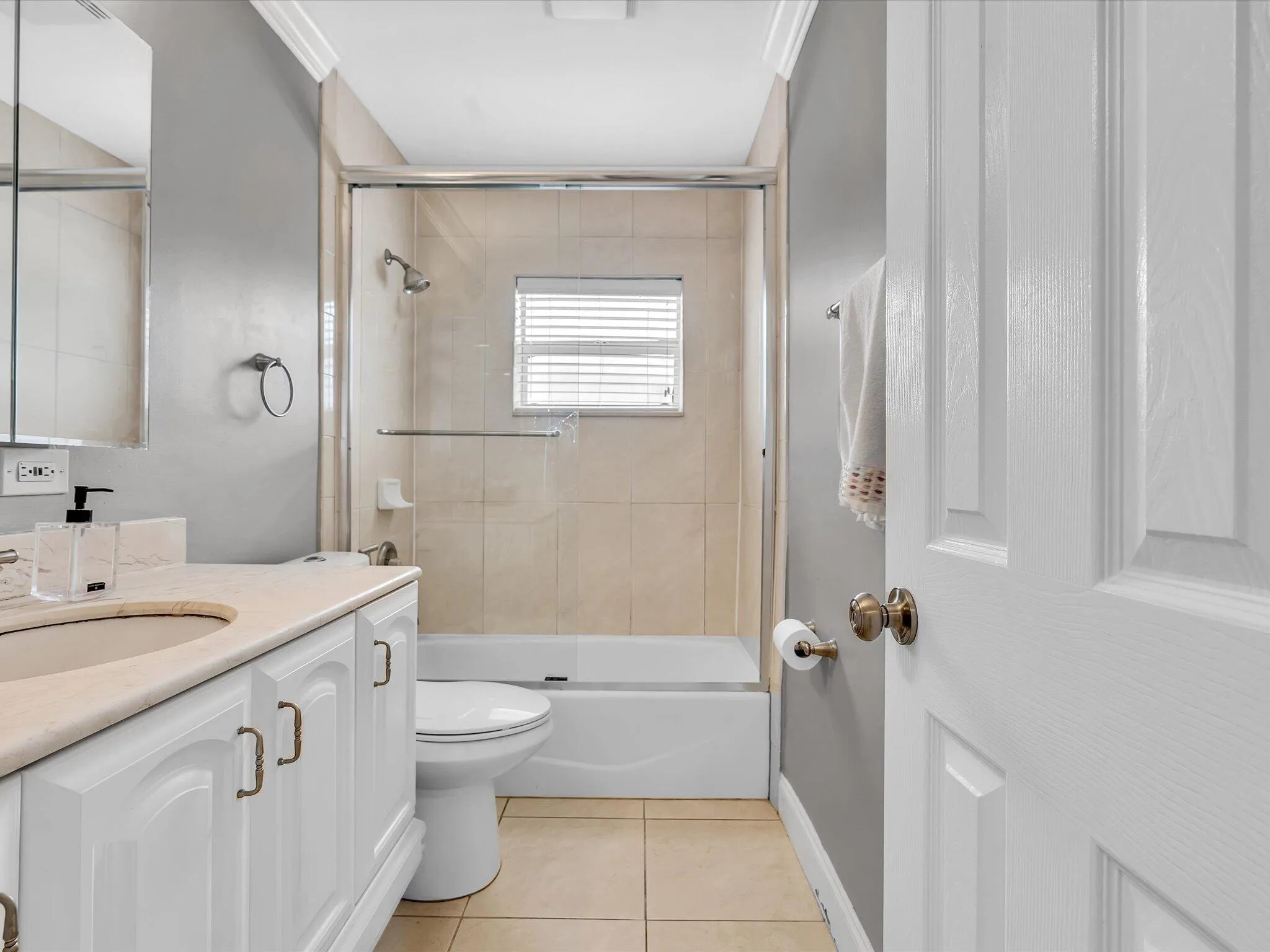 Bathroom featuring a white vanity with integrated sink, tiled flooring, a glass-enclosed tub/shower combination with tiled surround, and crown molding