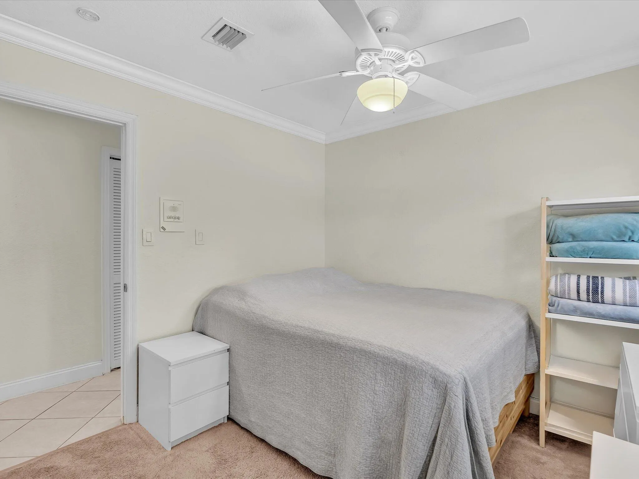 Bright secondary bedroom featuring neutral wall finishes, tile flooring, a ceiling fan with integrated lighting, and built-in shelving with storage