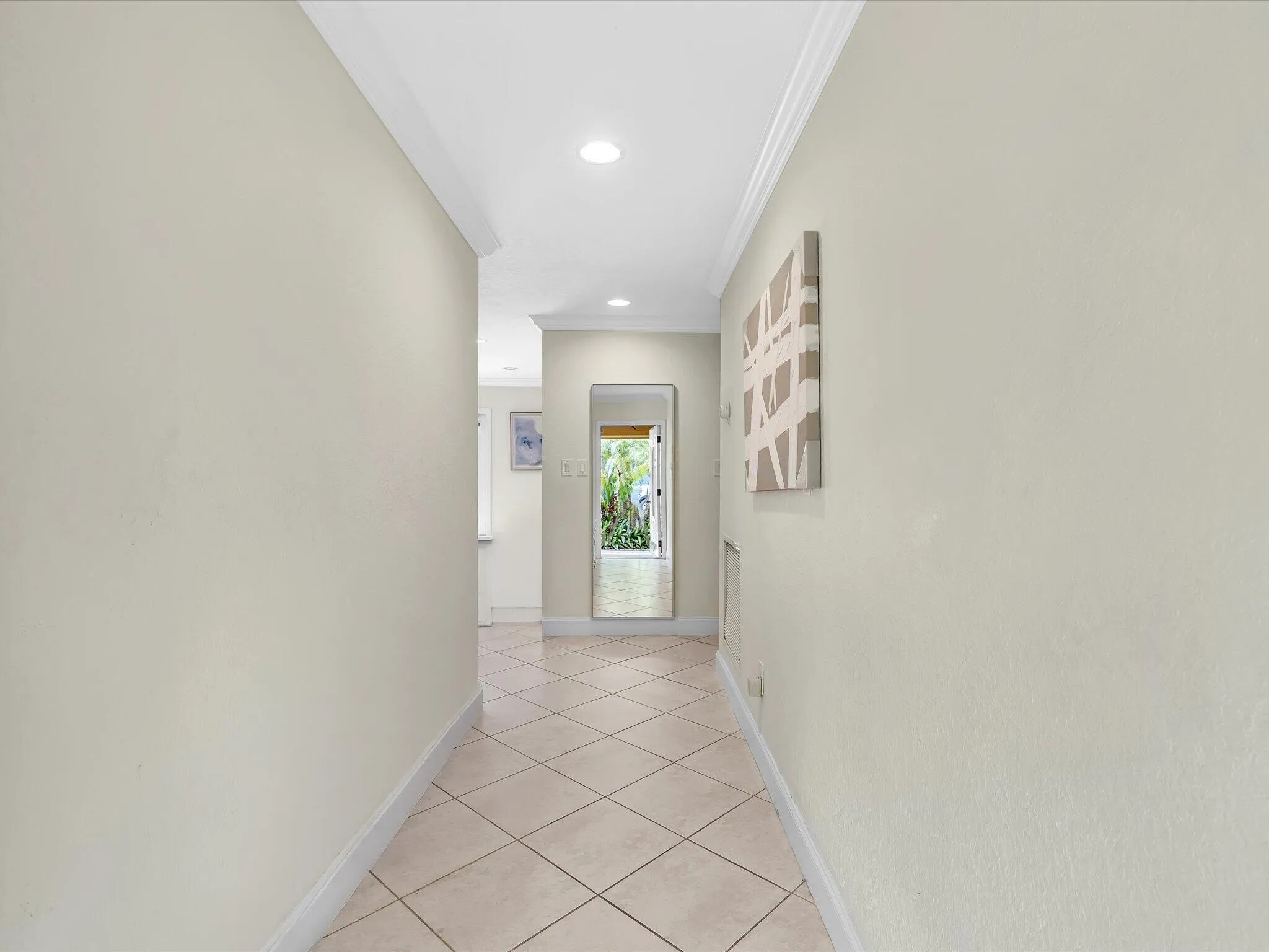 Recessed lighting illuminating a hallway with crown molding and diagonally laid tile flooring