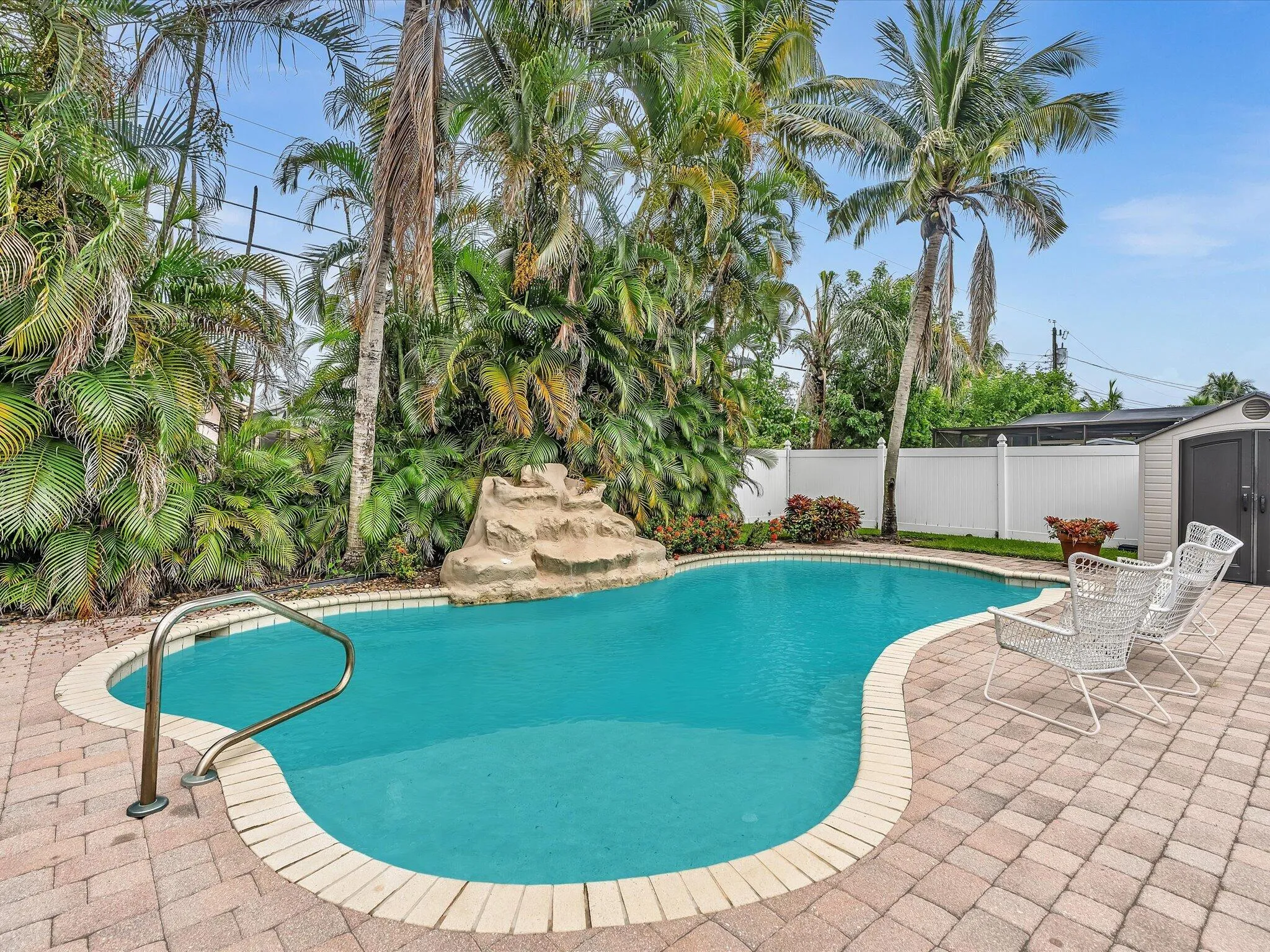 Freeform swimming pool with a rock waterfall feature, paver patio, and white privacy fencing