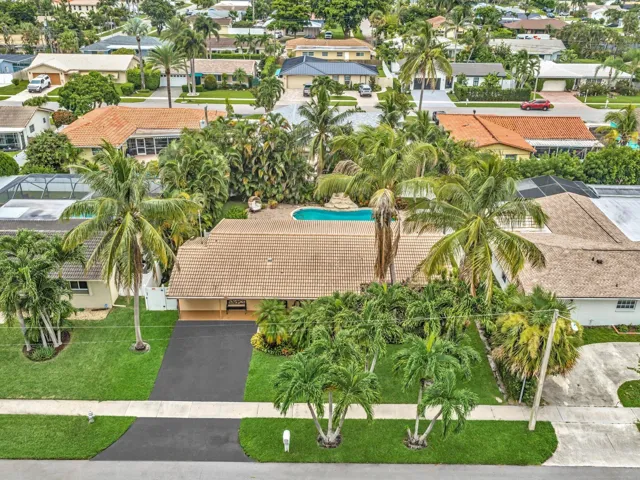 Expansive green lawn, mature palm trees, asphalt driveway, exterior light brown tile roof, and a visible swimming pool