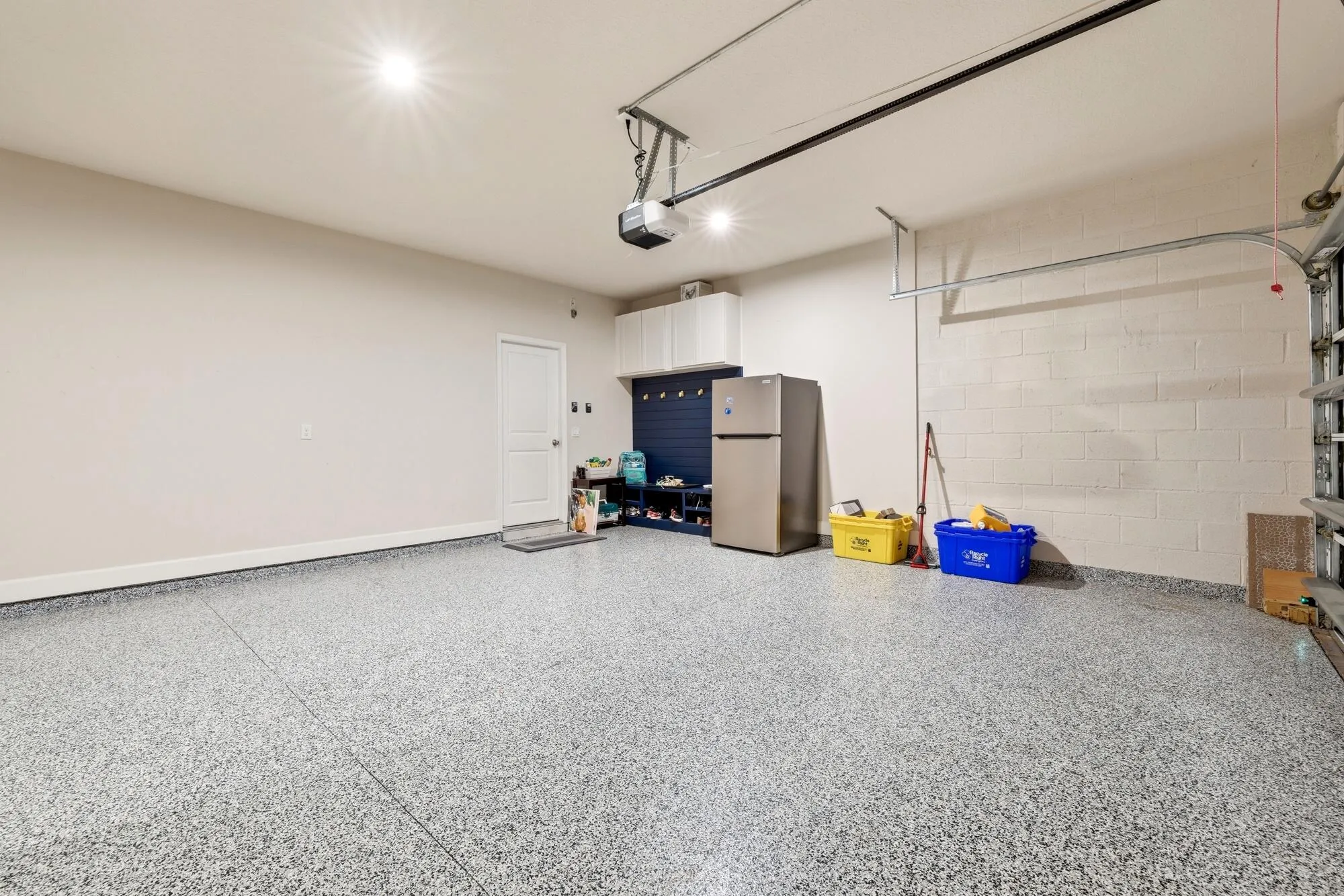 Spacious three car garage with epoxy-coated flooring, overhead garage door opener, recessed lighting, built-in cabinetry, and painted cinder block walls