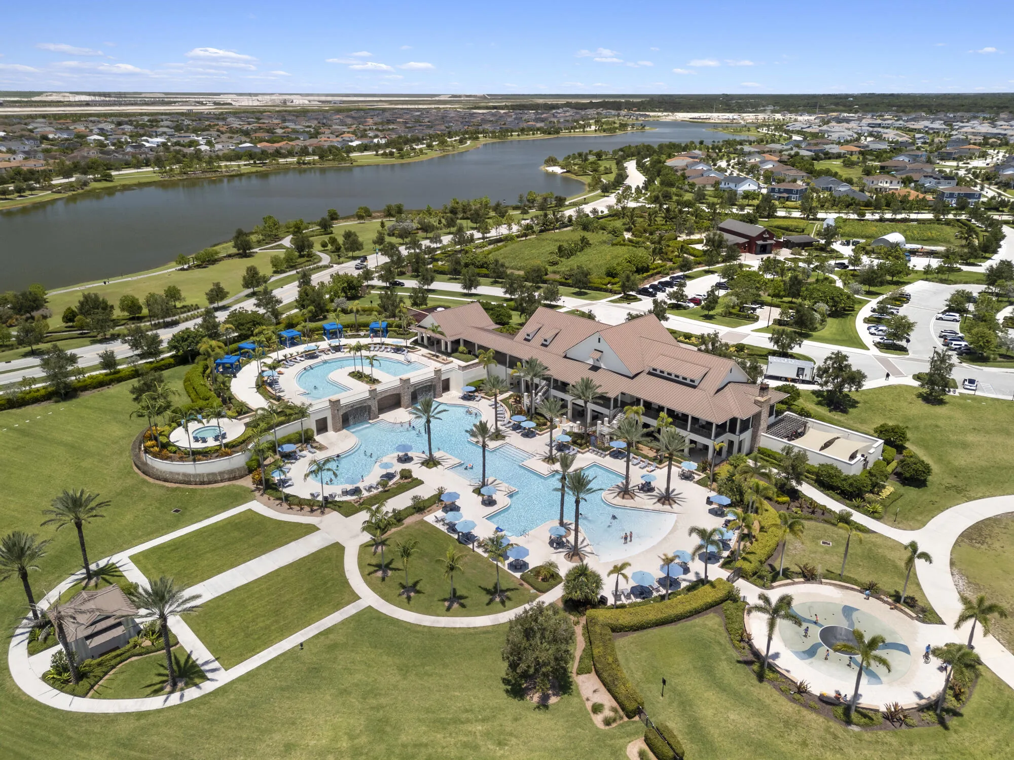 Expansive community clubhouse featuring a multi-level pool complex, a separate splash pad, and surrounding lush green spaces with mature palm trees