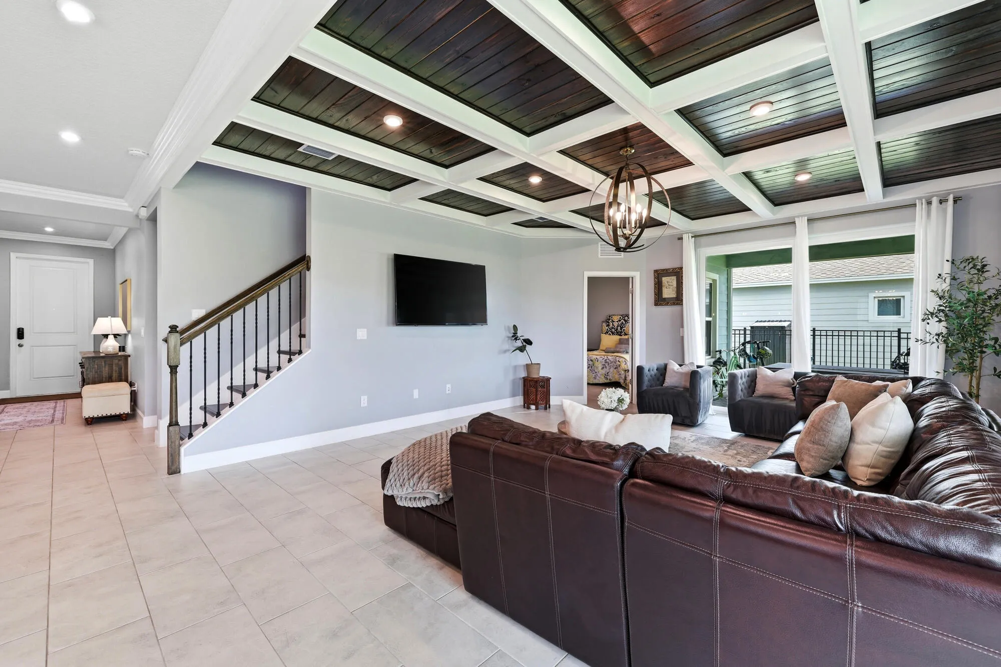 Spacious living area featuring a wood-finish coffered ceiling with recessed lighting, large format tile flooring, and oversized windows