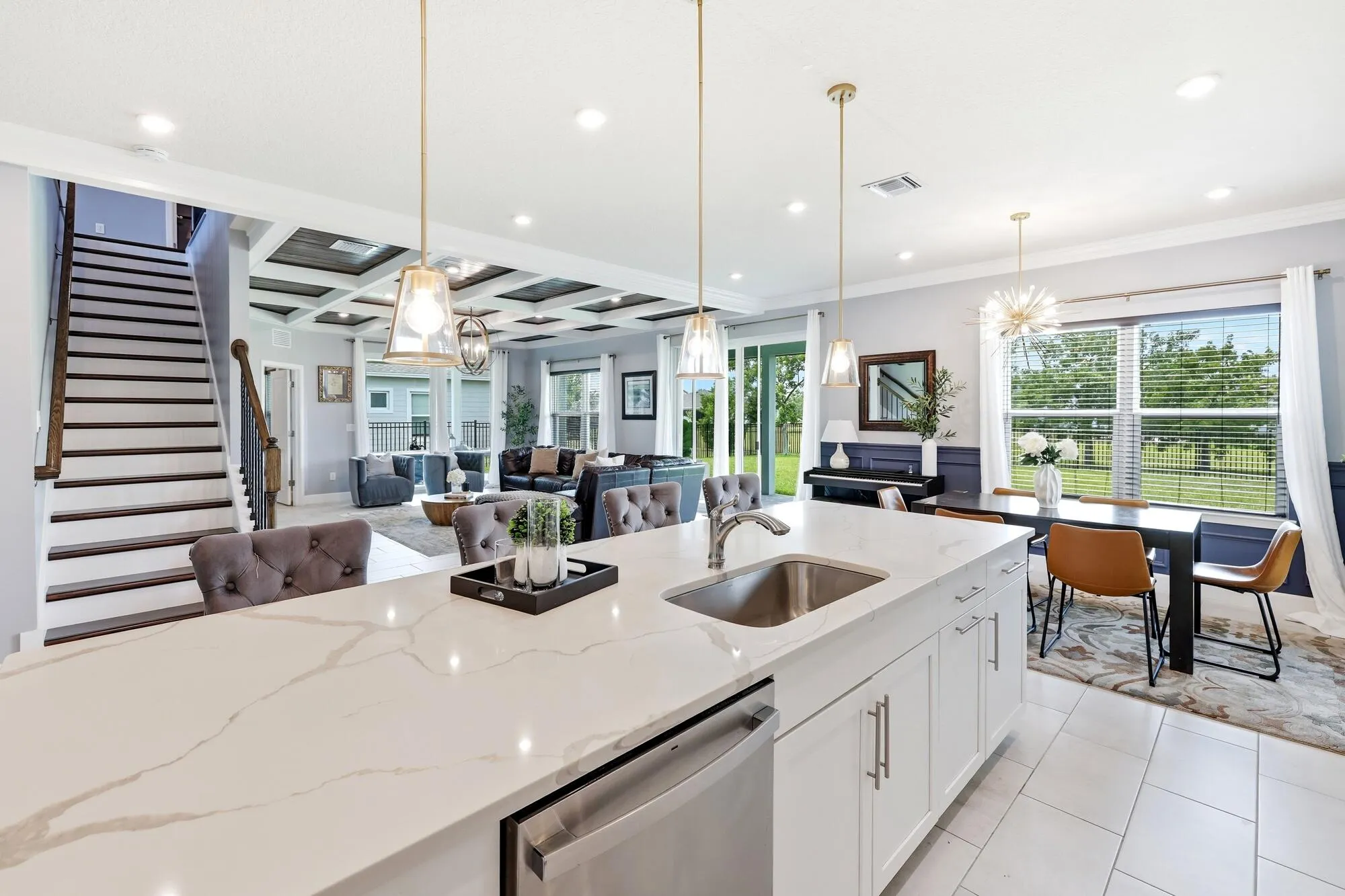 Kitchen island featuring a stainless steel sink, white cabinetry, and a light-toned quartz countertop with veining