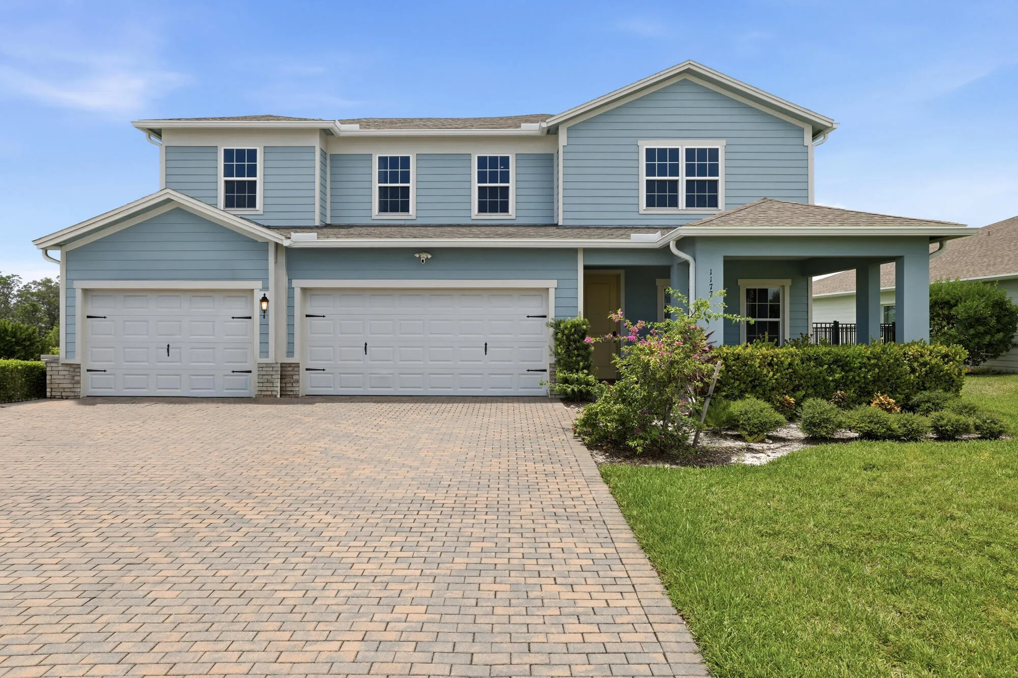 Two-story residence featuring light blue siding, a covered front porch, and a two-car garage with white doors