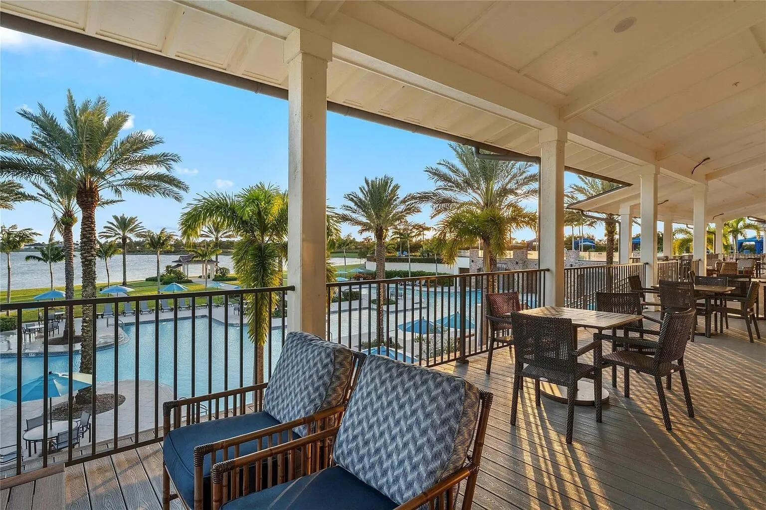 Covered clubhouse veranda with comfortable seating overlooking the resort-style pool and community lake — the perfect spot to unwind at sunset.
