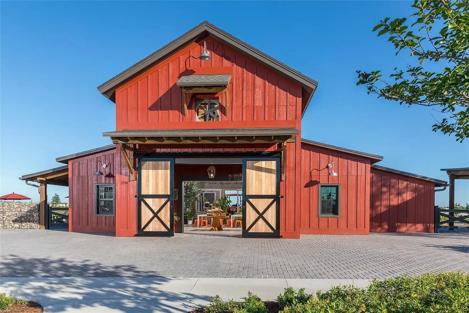 Community farmhouse-style market and event barn with rustic red board-and-batten exterior, oversized barn doors, and covered outdoor gathering space — a signature amenity for this master-planned community.