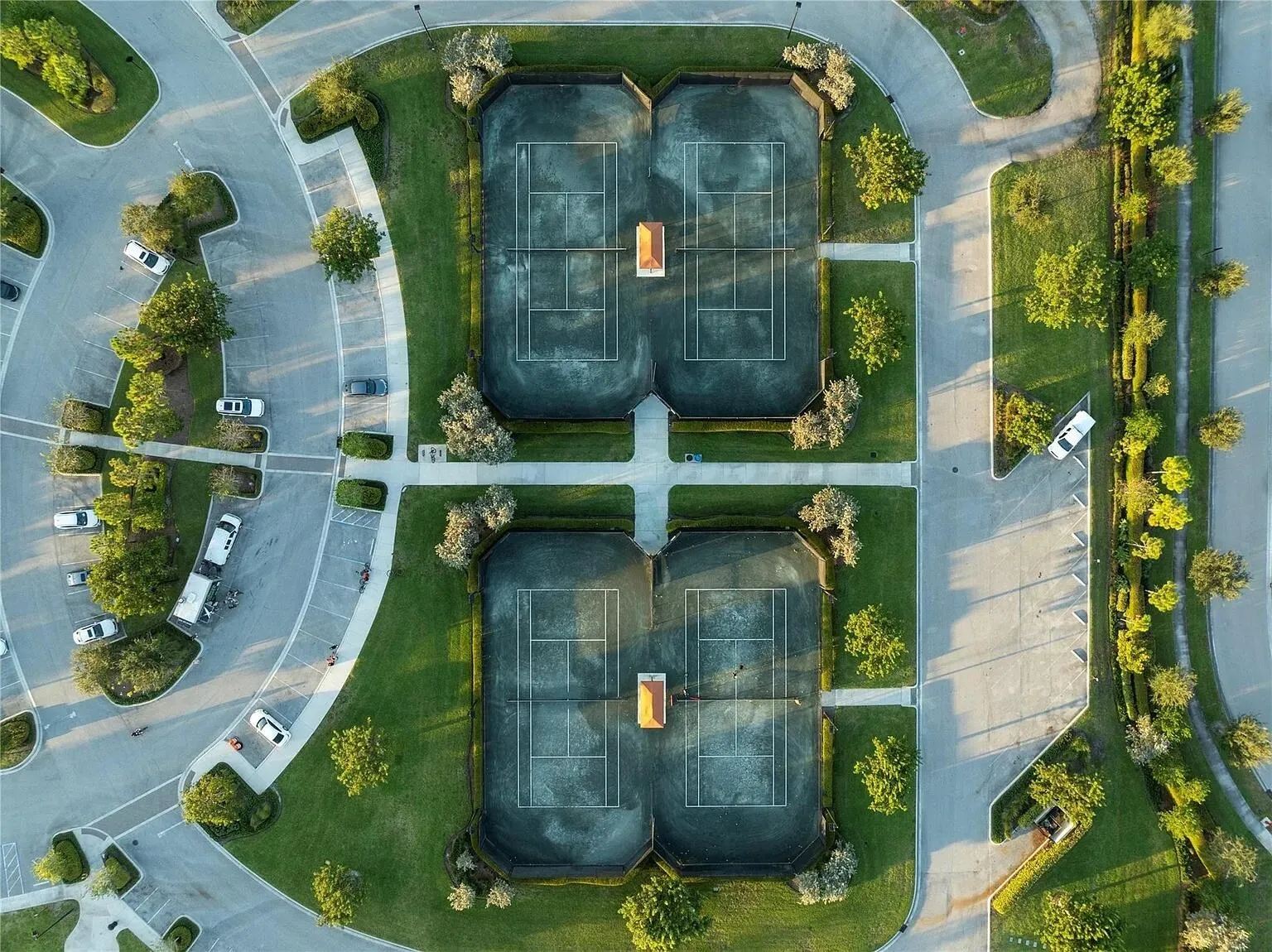 Aerial view of the community's four lighted tennis and pickleball courts, surrounded by lush landscaping and ample parking — a dream setup for active lifestyle buyers.
