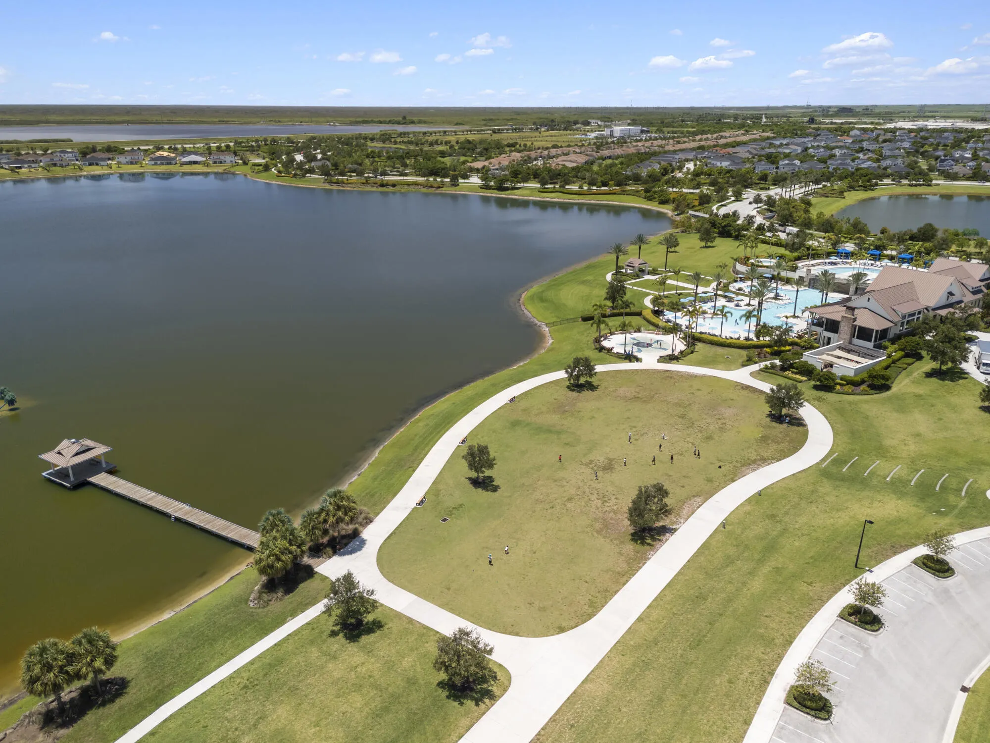 Expansive waterfront community featuring a large lake, a recreational clubhouse with multiple pools, a private dock with a covered gazebo, and paved walking paths