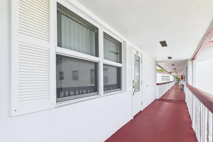Bright corridor featuring expansive windows with operable shutters, continuous red flooring, white wall paneling, and recessed ceiling lighting
