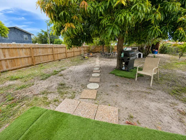 A charming stepping-stone path winds beneath a mature mango tree, connecting the patio grill area to the fire pit — a shaded outdoor living space ready to enjoy.