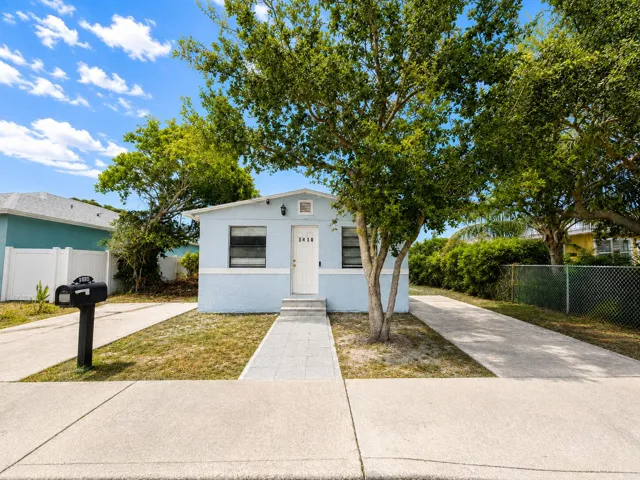 ight blue cottage with crisp white trim, a mature shade tree framing the entryway, and a tidy paver walkway leading to the front door — inviting curb appeal