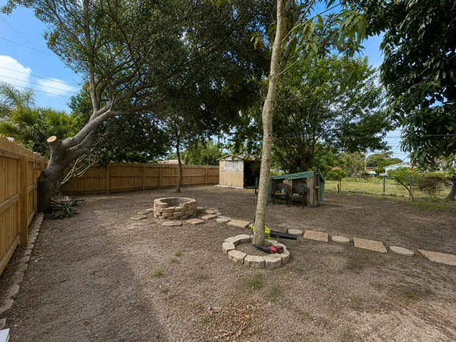 Backyard fire pit surrounded by a stone paver seating area, perfect for gathering with friends and family under the natural tree canopy. The fully fenced yard offers privacy and room to roam.